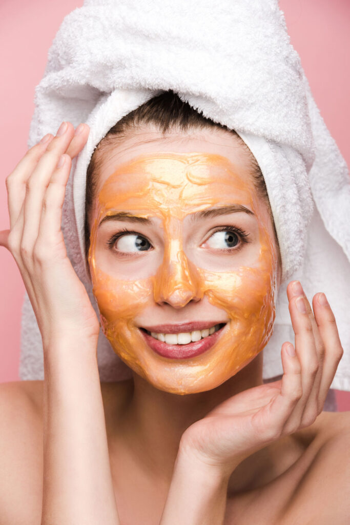 Cheerful girl with facial mask and towel on head holding hands n