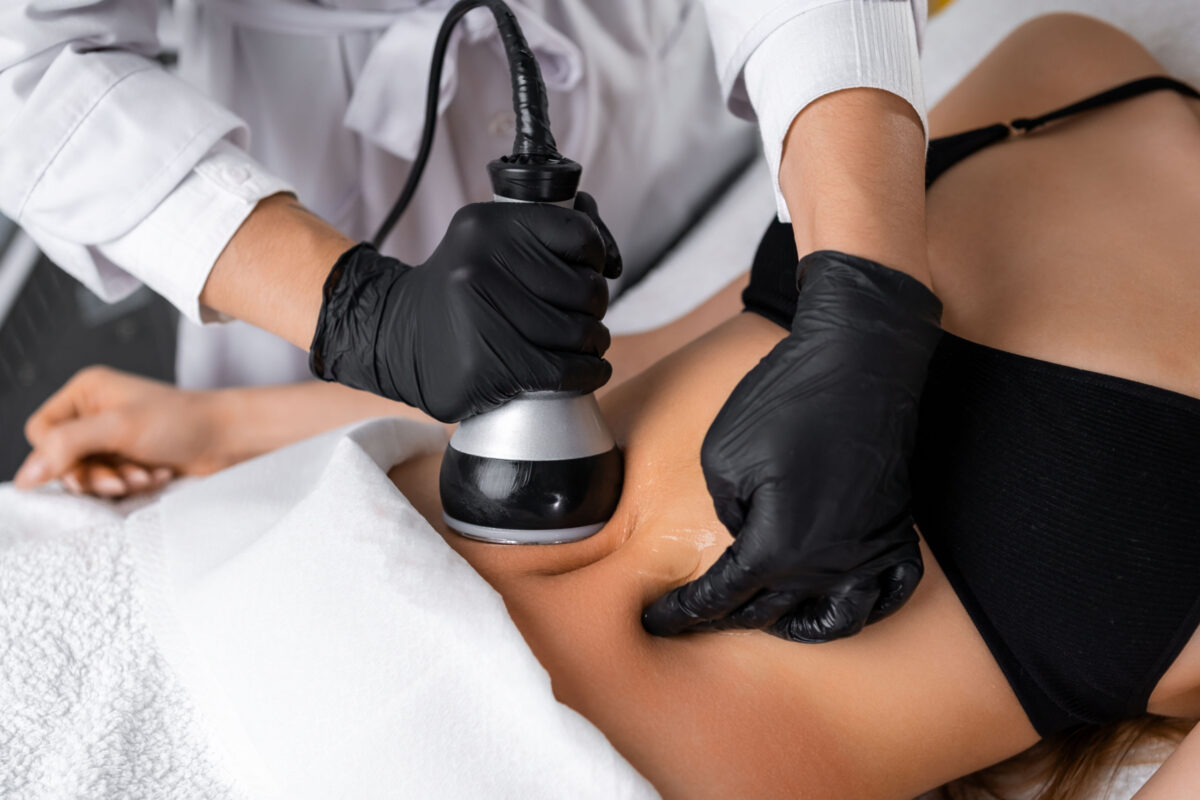 A cosmetologist utilizes an ultrasound device during a lifting procedure on a woman's abdomen.