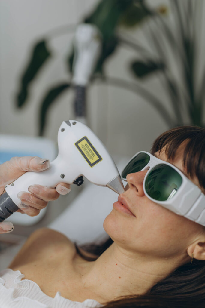 Professional cosmetologist performing facial laser hair removal on woman wearing protective glasses