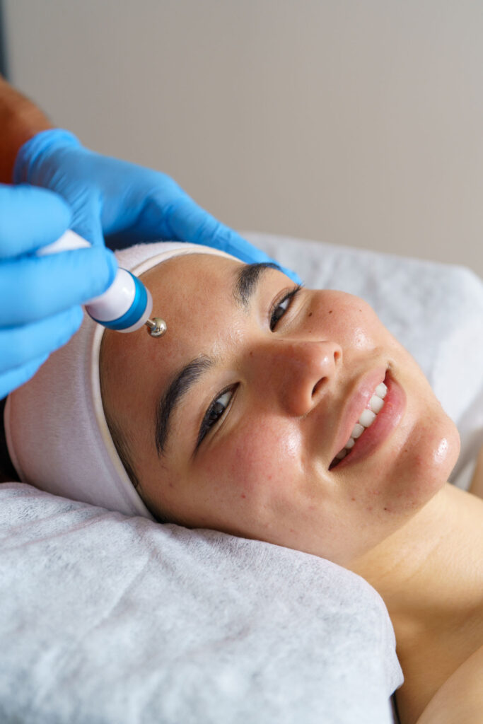 Professional beautician applying advanced facial treatment, rejuvenating smiling client during luxurious spa skincare session